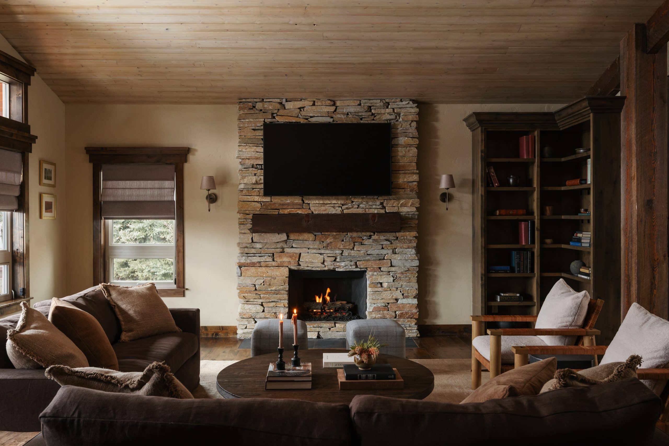 Living room with dry-stacked stone fireplace, wood-plank ceiling, and built-in bookshelves