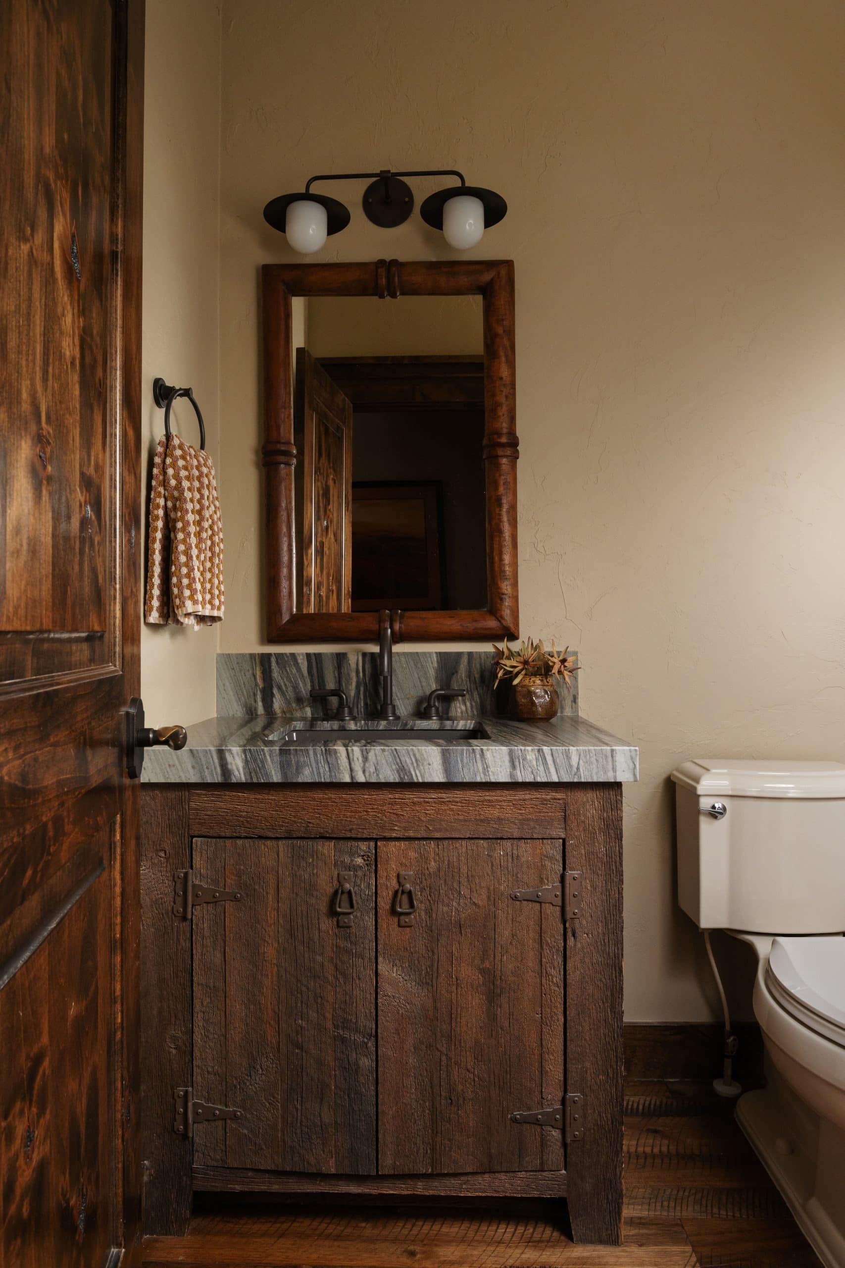 Powder room with a rustic reclaimed-wood vanity, stone countertop, and framed mirror