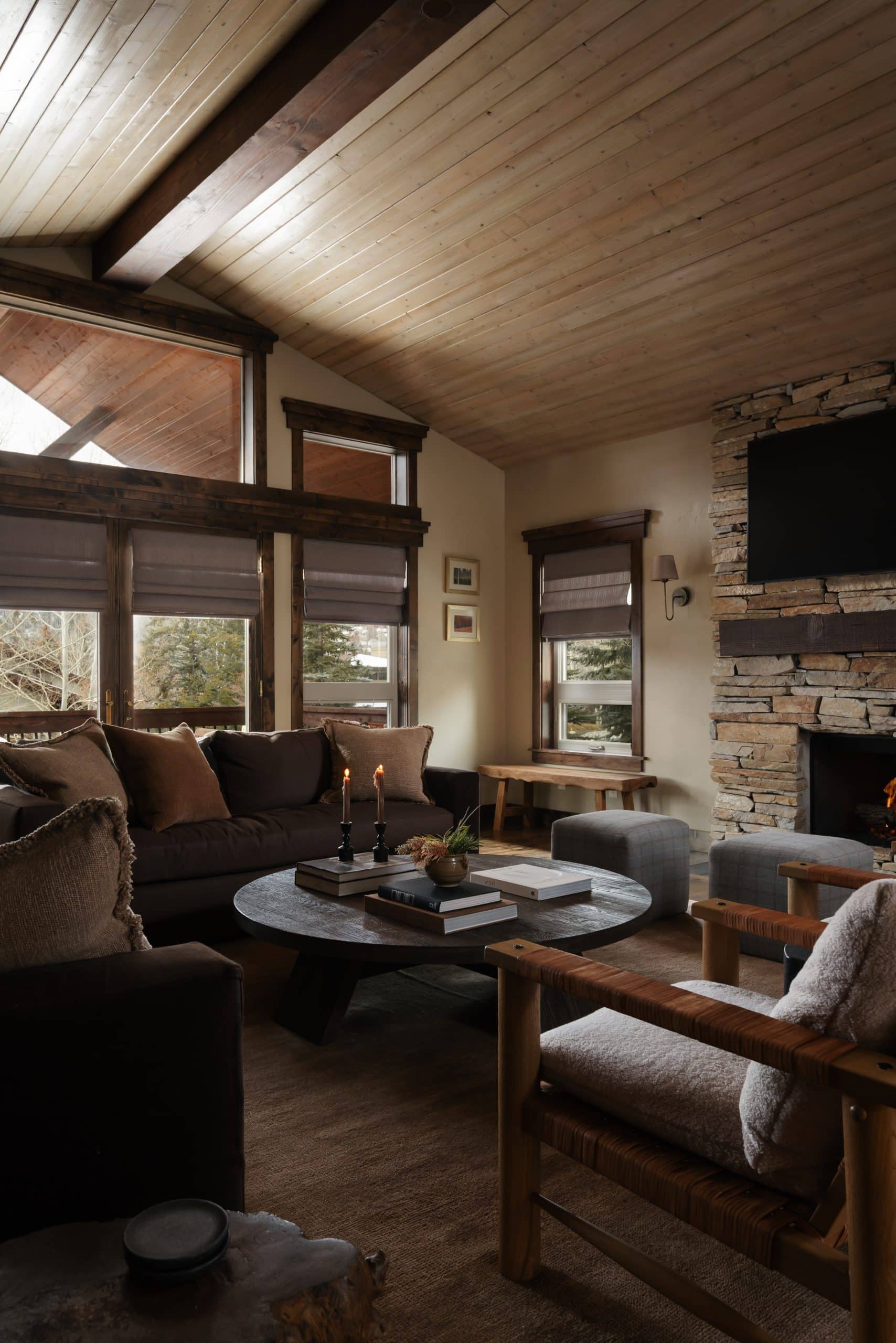 Living room with vaulted wood ceiling, stone fireplace, and deep brown upholstered seating