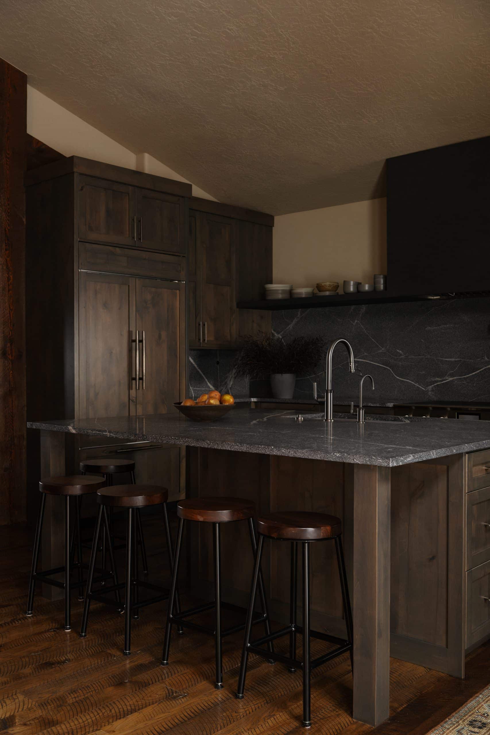 Kitchen with stained-wood cabinetry, dark stone backsplash, and counter stools at a stone-topped island
