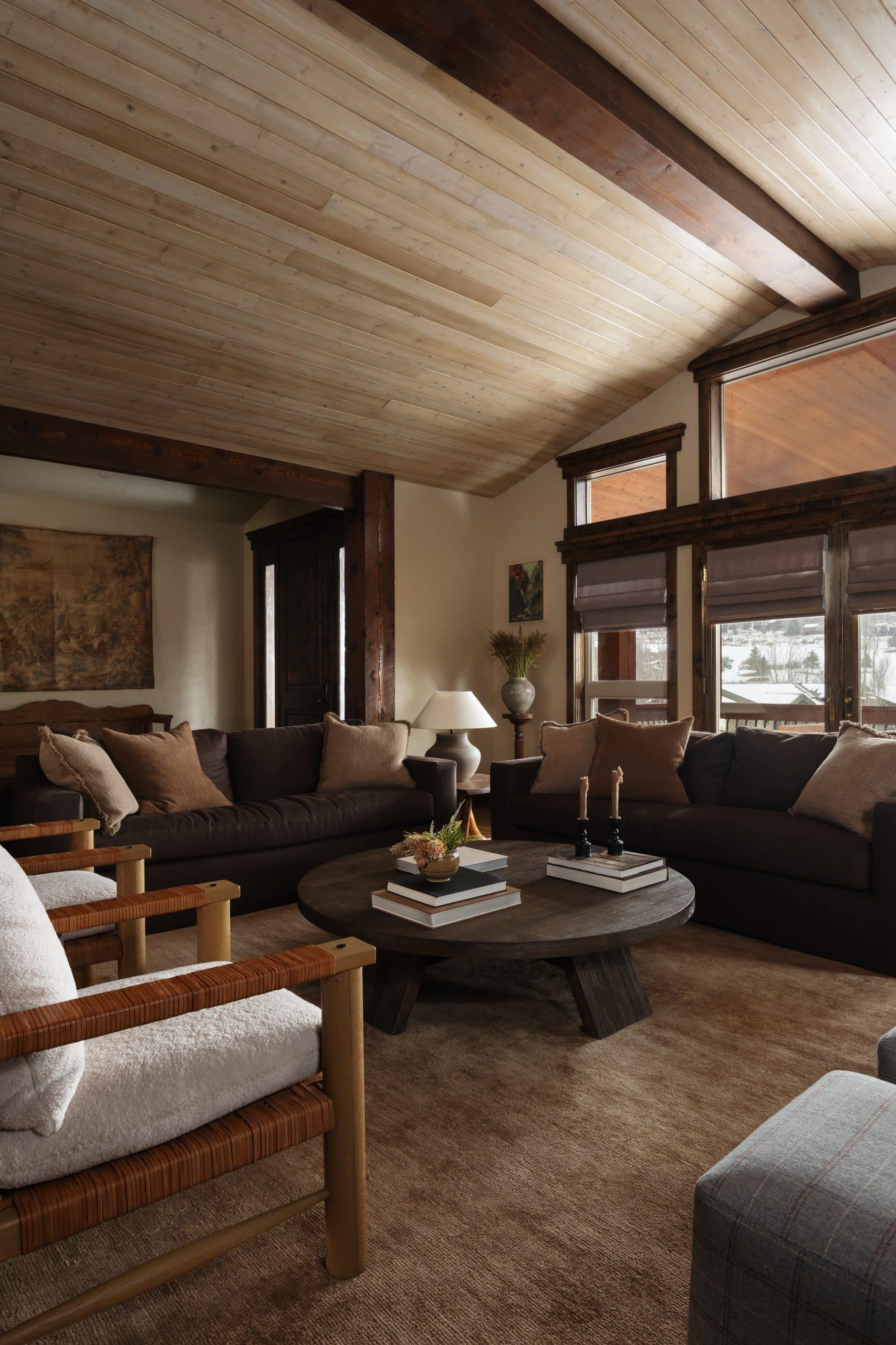 Family room with brown sofas, woven-leather chairs, and a round wood coffee table under a beamed ceiling