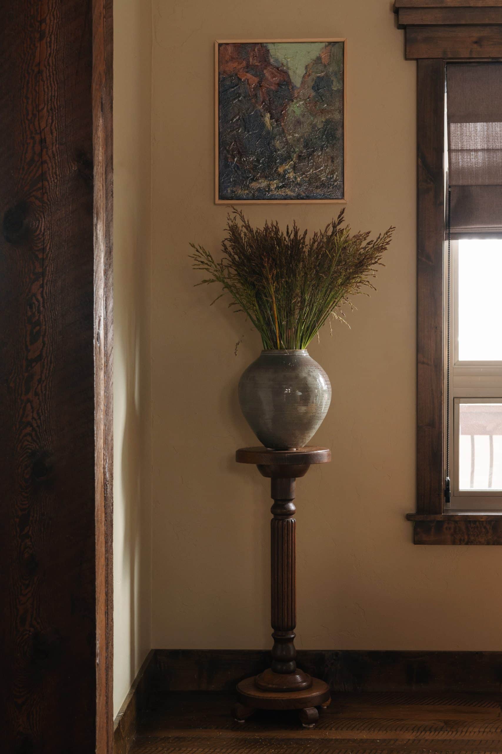 Entry vignette with an abstract landscape painting above a ceramic vase of dried grasses on a turned-wood pedestal