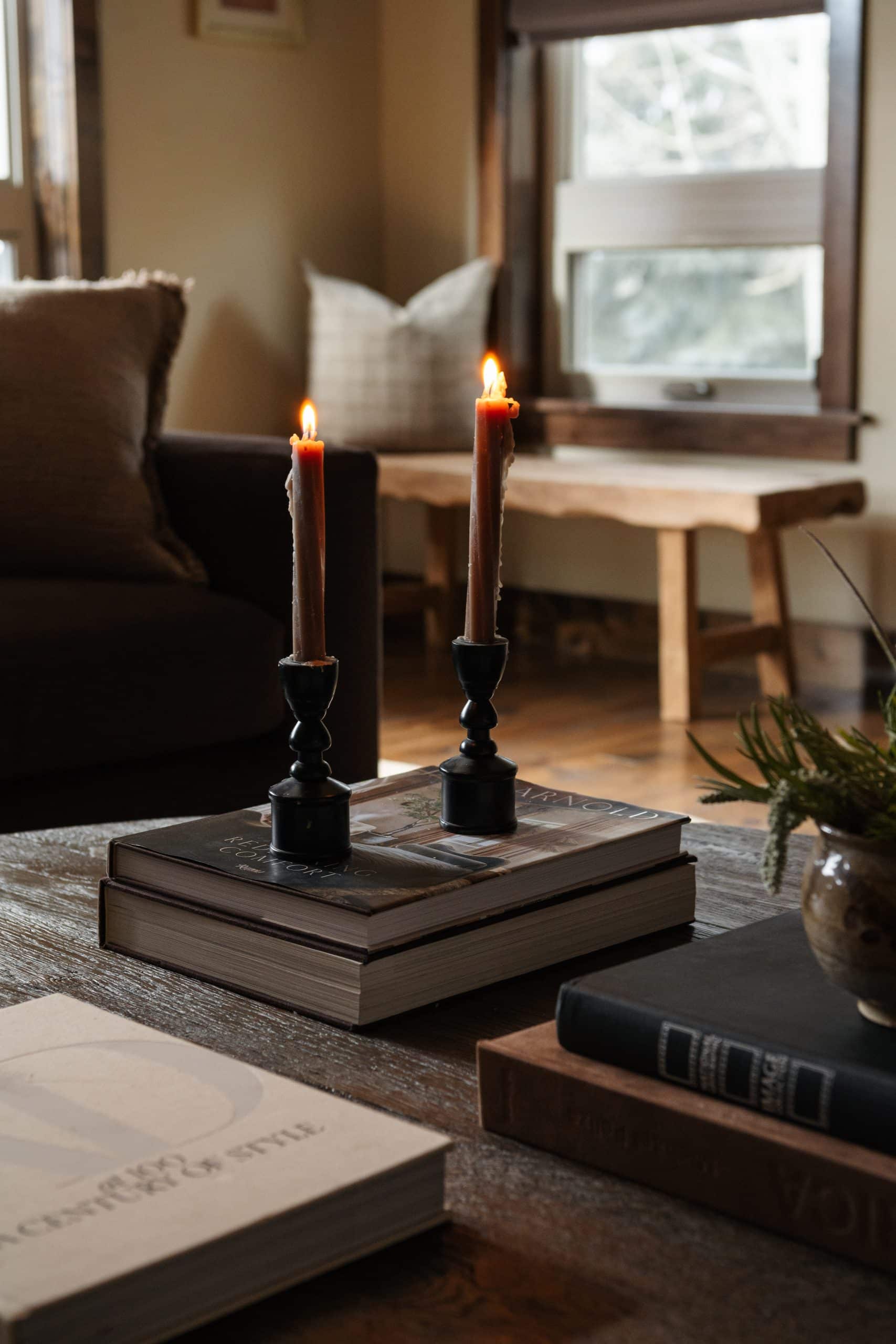 Coffee table styled with black taper candles and stacked design books beside a live-edge bench