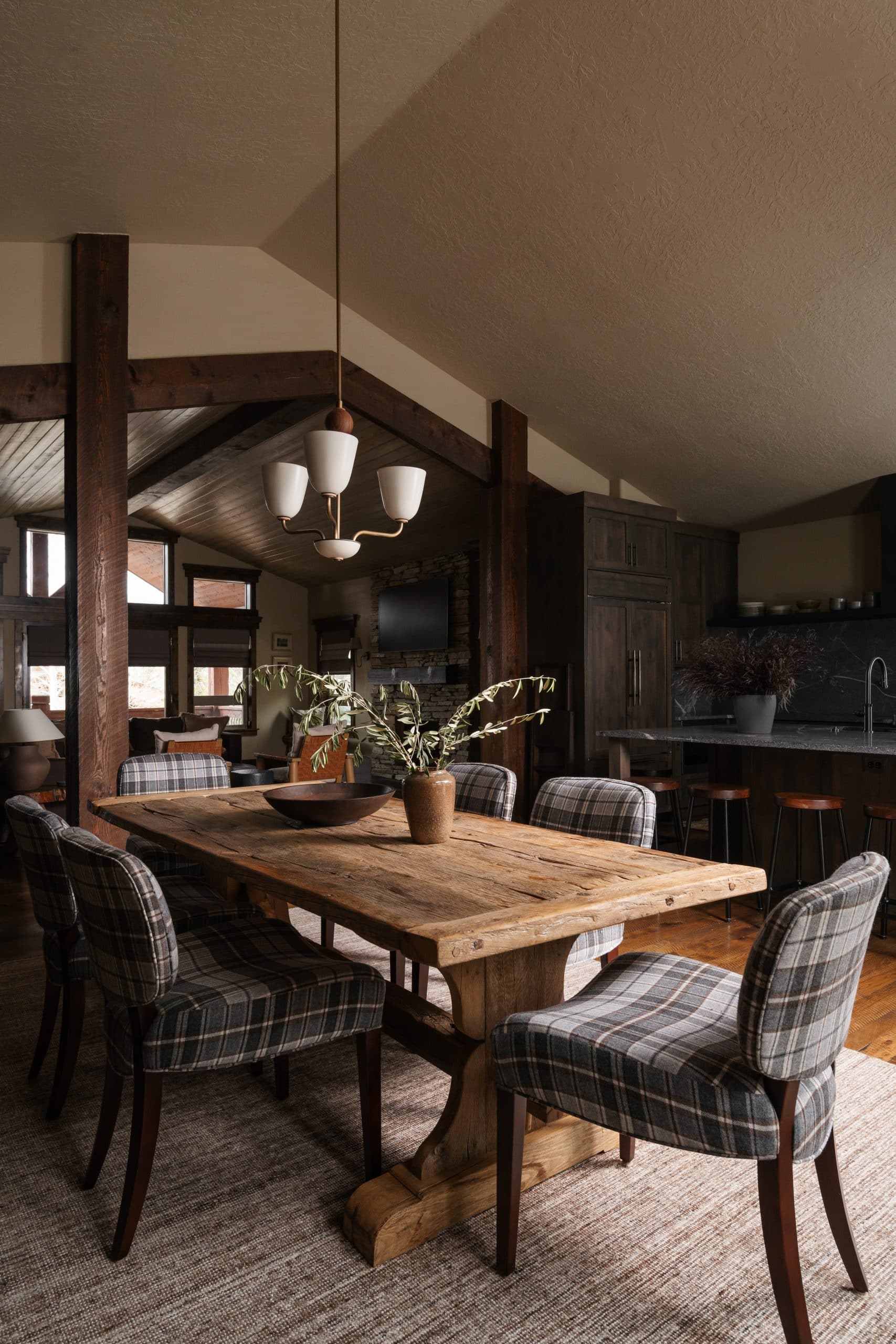 Mountain modern dining room with a reclaimed-wood table, plaid chairs, and exposed timber beams
