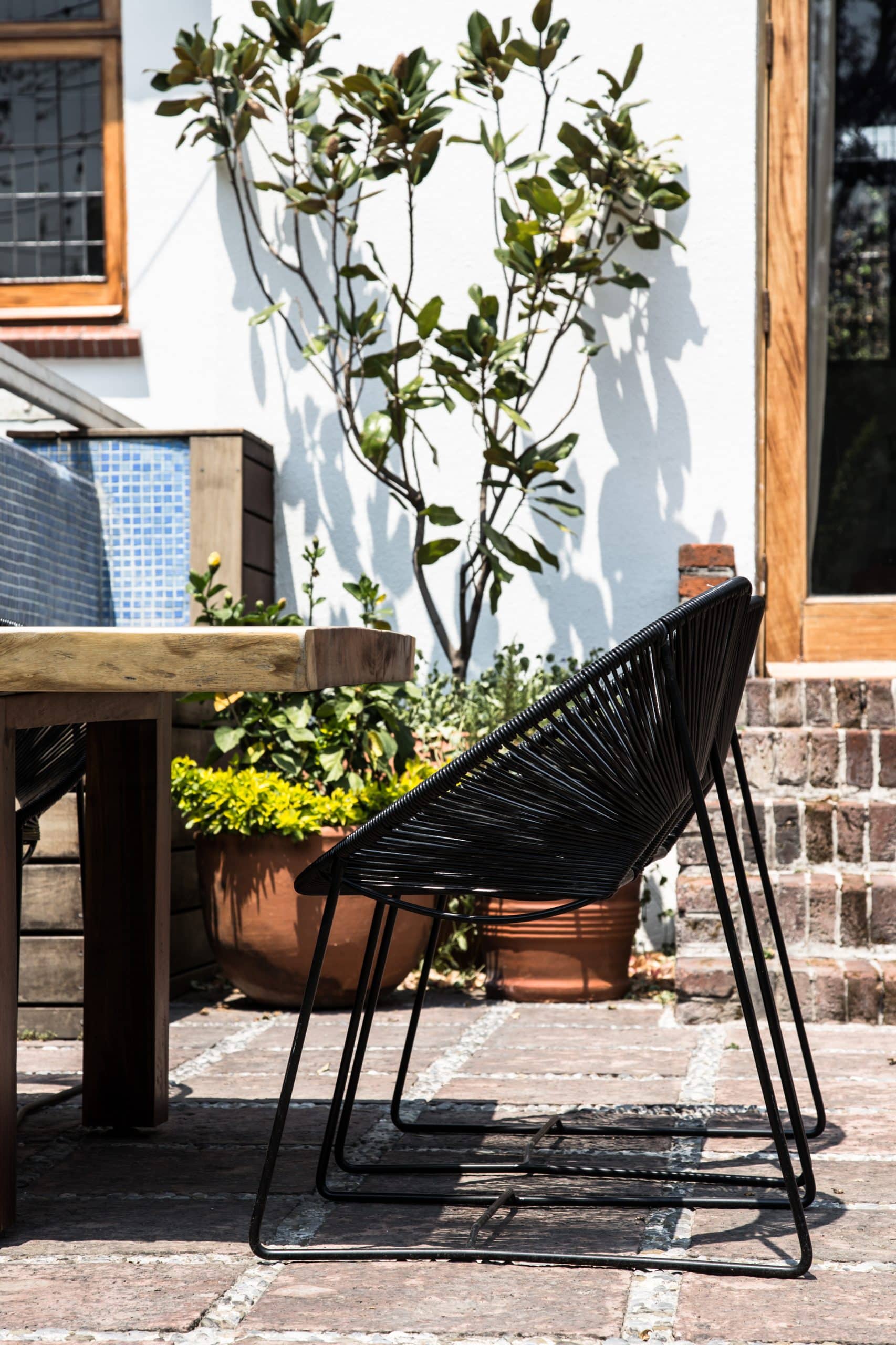 Custom black Acapulco chair and live-edge wood dining table on terracotta pavers