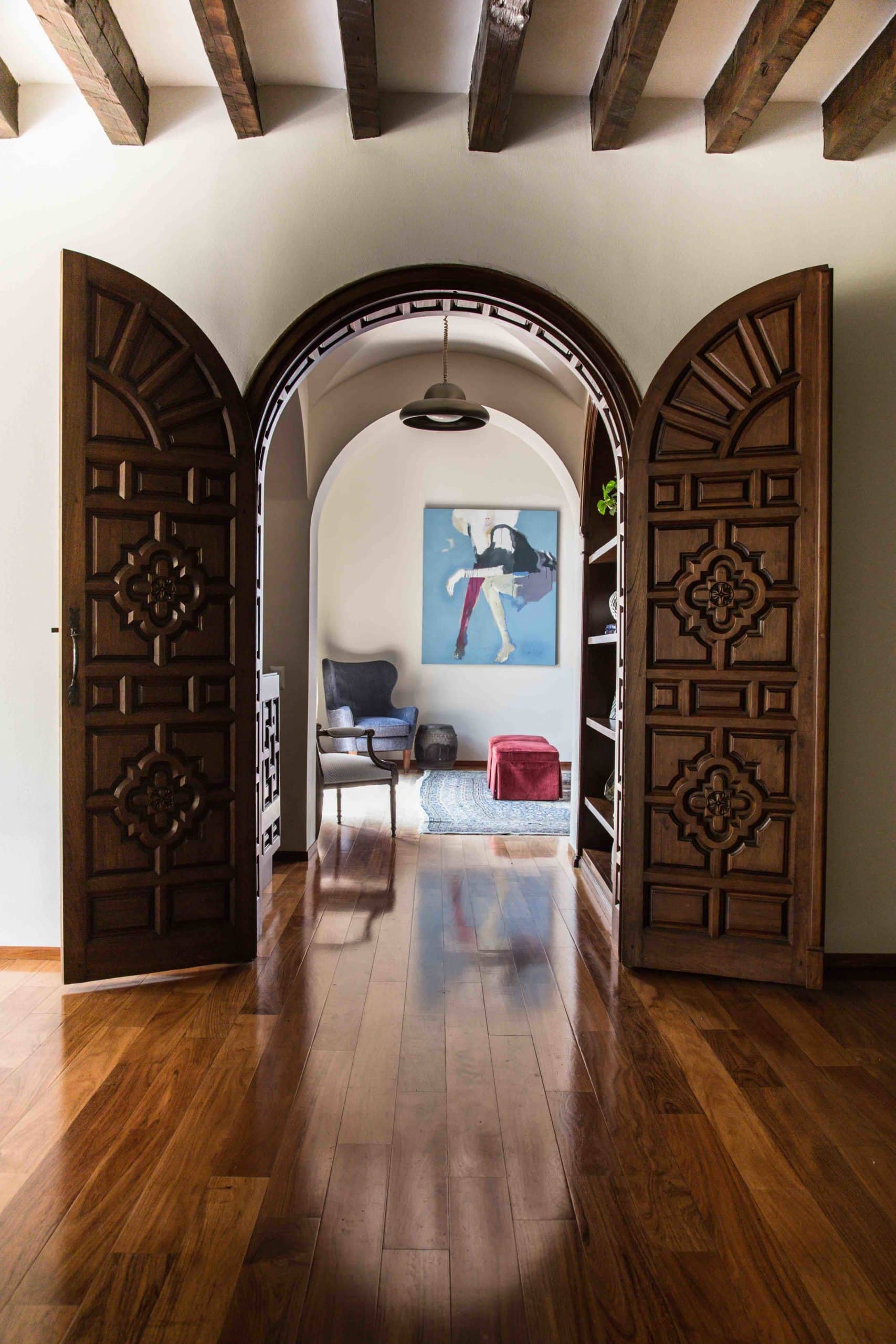 Handcarved arched wooden doors opening to a living room with contemporary art and exposed beams