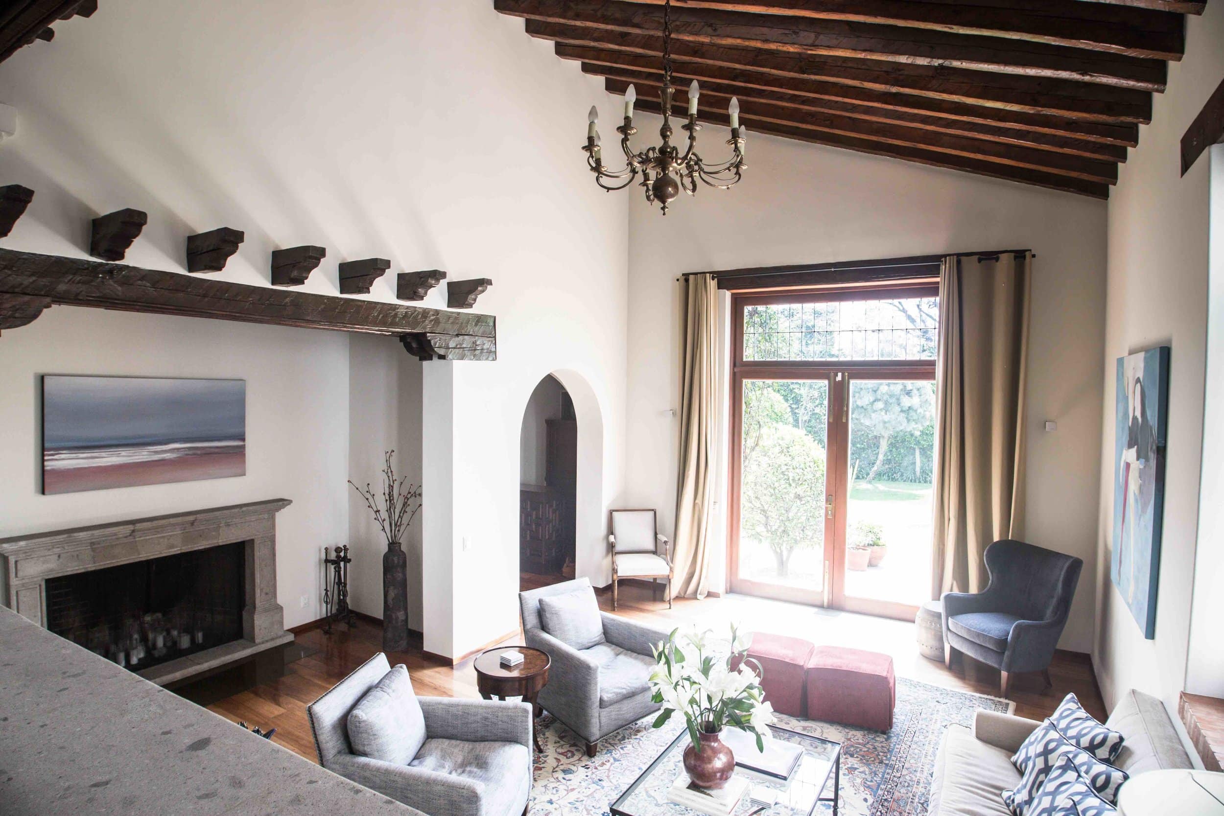 Living room with stone fireplace, exposed wood beams, and garden views through French doors