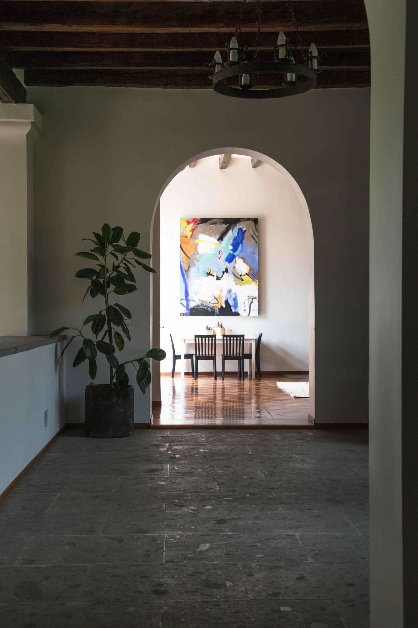 Stone-floored hallway with an arched entry framing abstract art under a wood beam ceiling