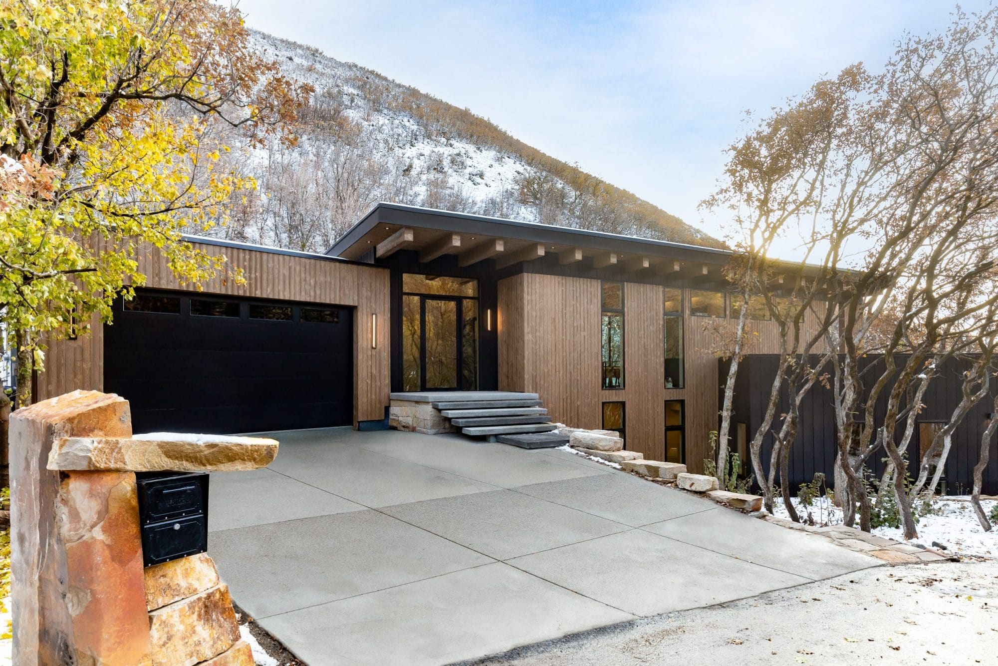 Front exterior of the wood-clad modern home with a black garage door against a snow-dusted mountainside
