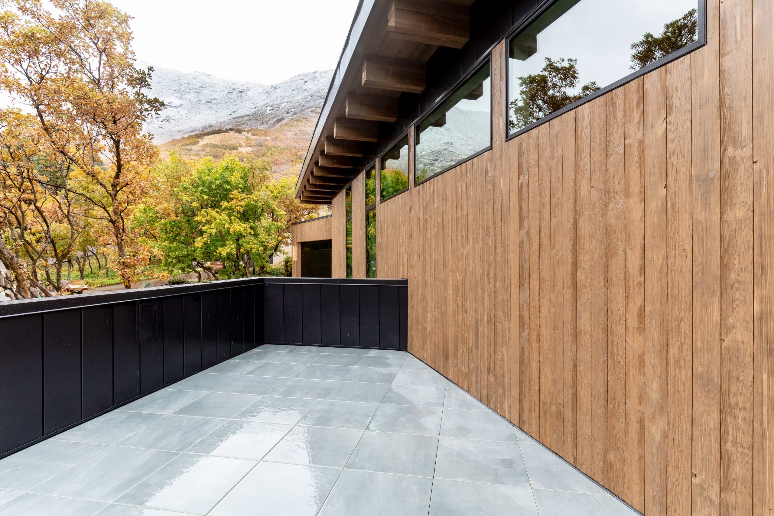 Stone-tiled deck bordered by black planters, wood siding, and a view toward autumn hillsides