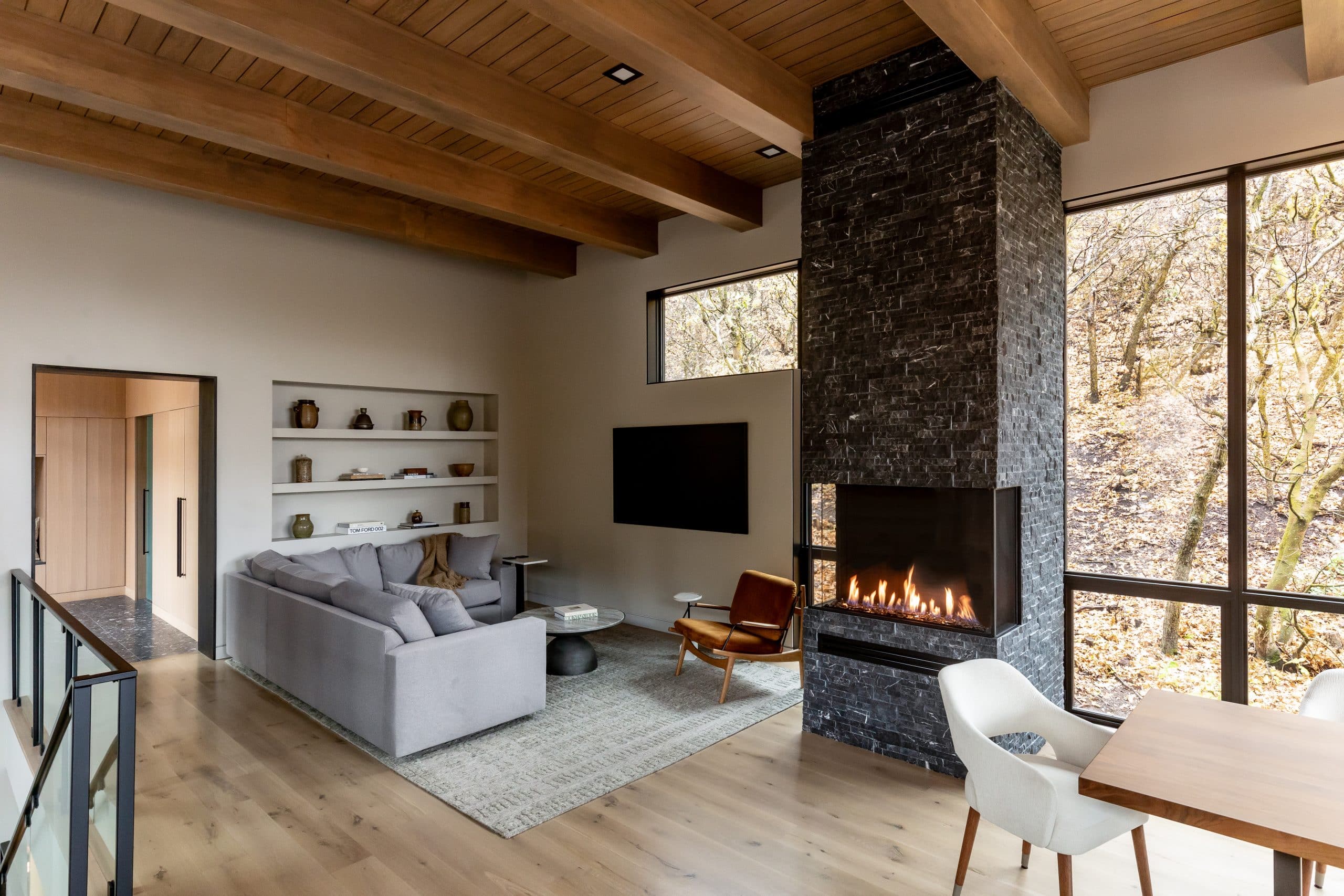 Living and dining space with a tall black stone fireplace, leather chair, and dining table by the windows