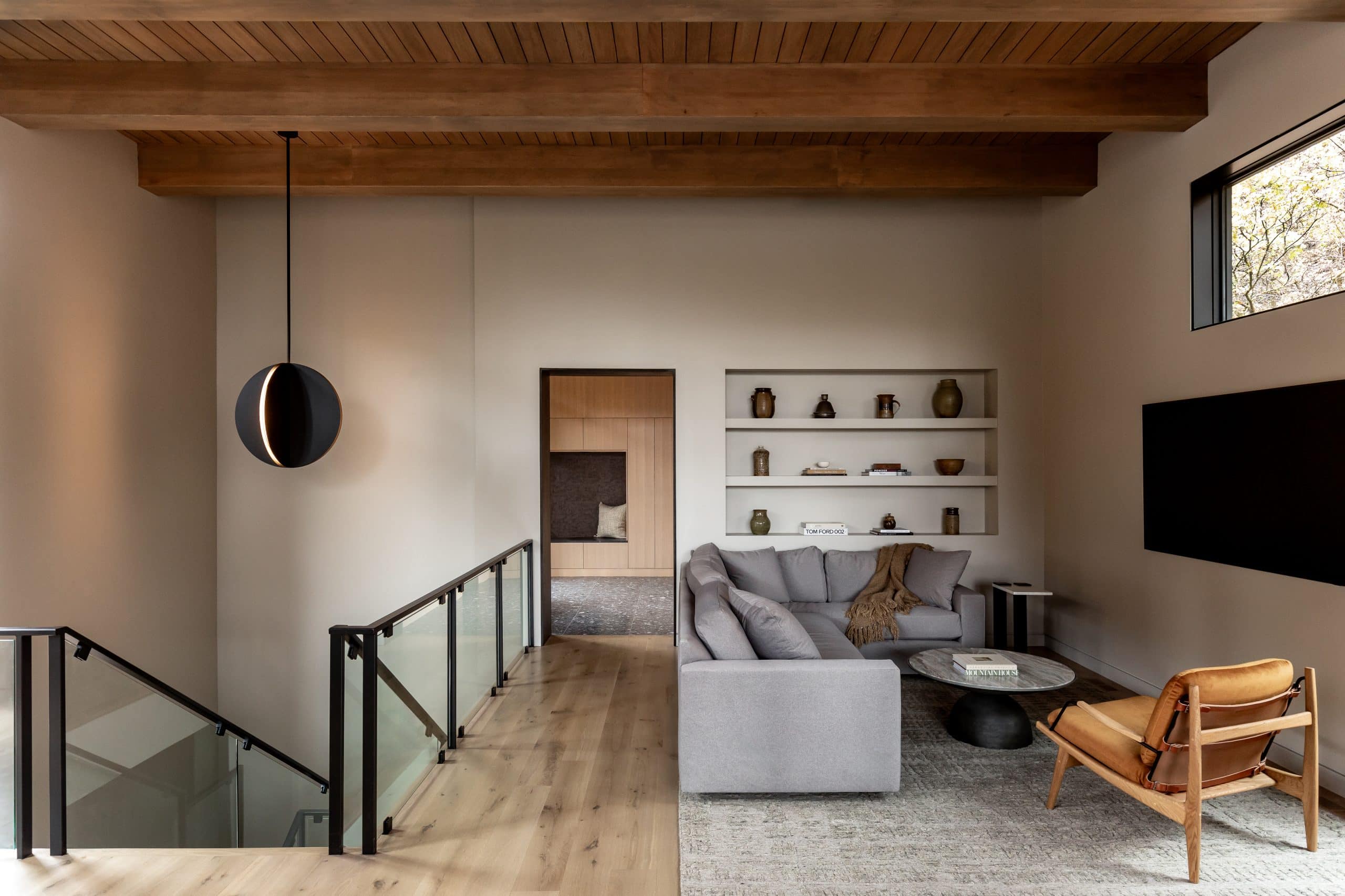Upstairs sitting area with a gray sofa, leather chair, and recessed shelving under a wood-beam ceiling