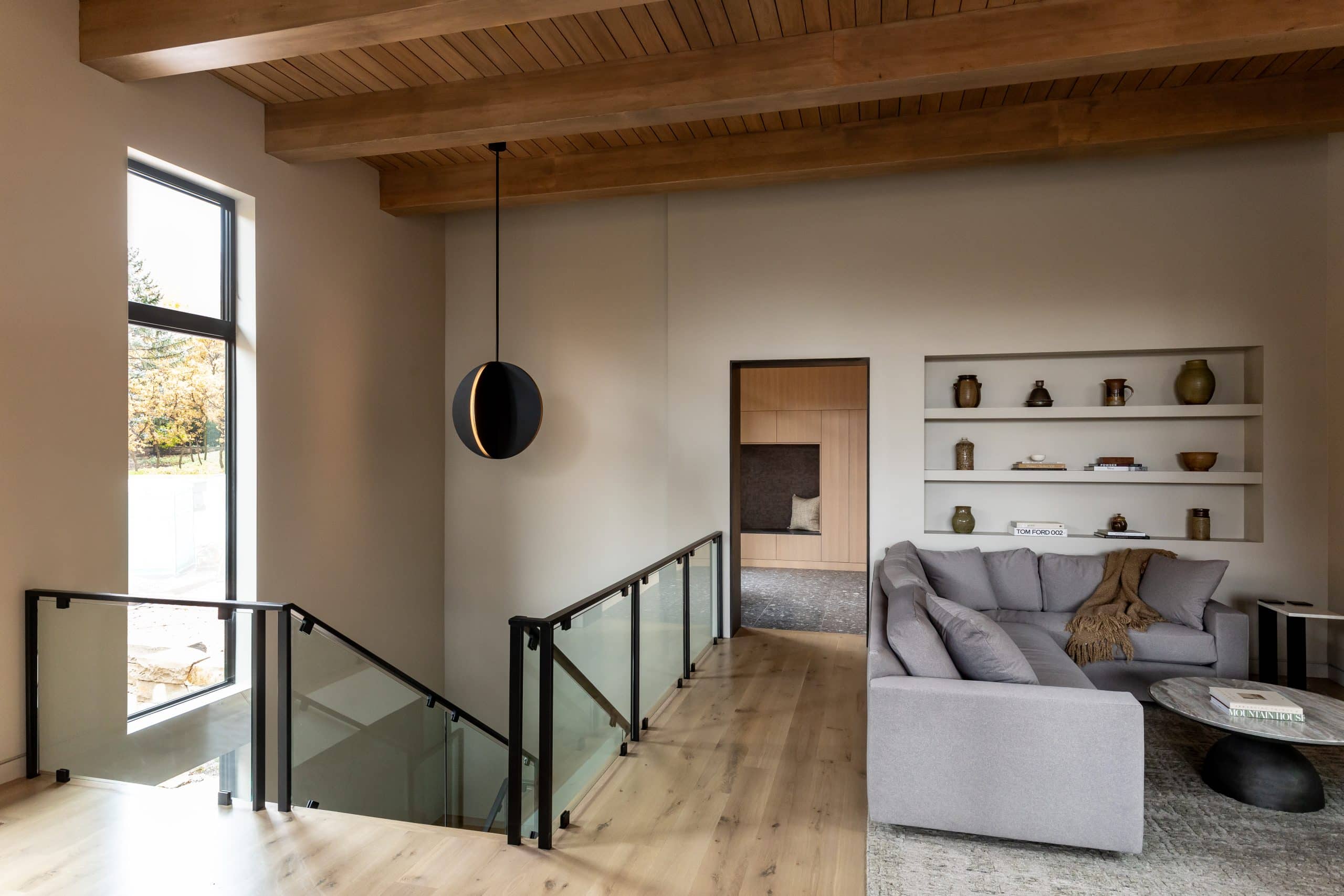 Stair landing with a sculptural black pendant, glass rail, and a gray sectional beside recessed shelves