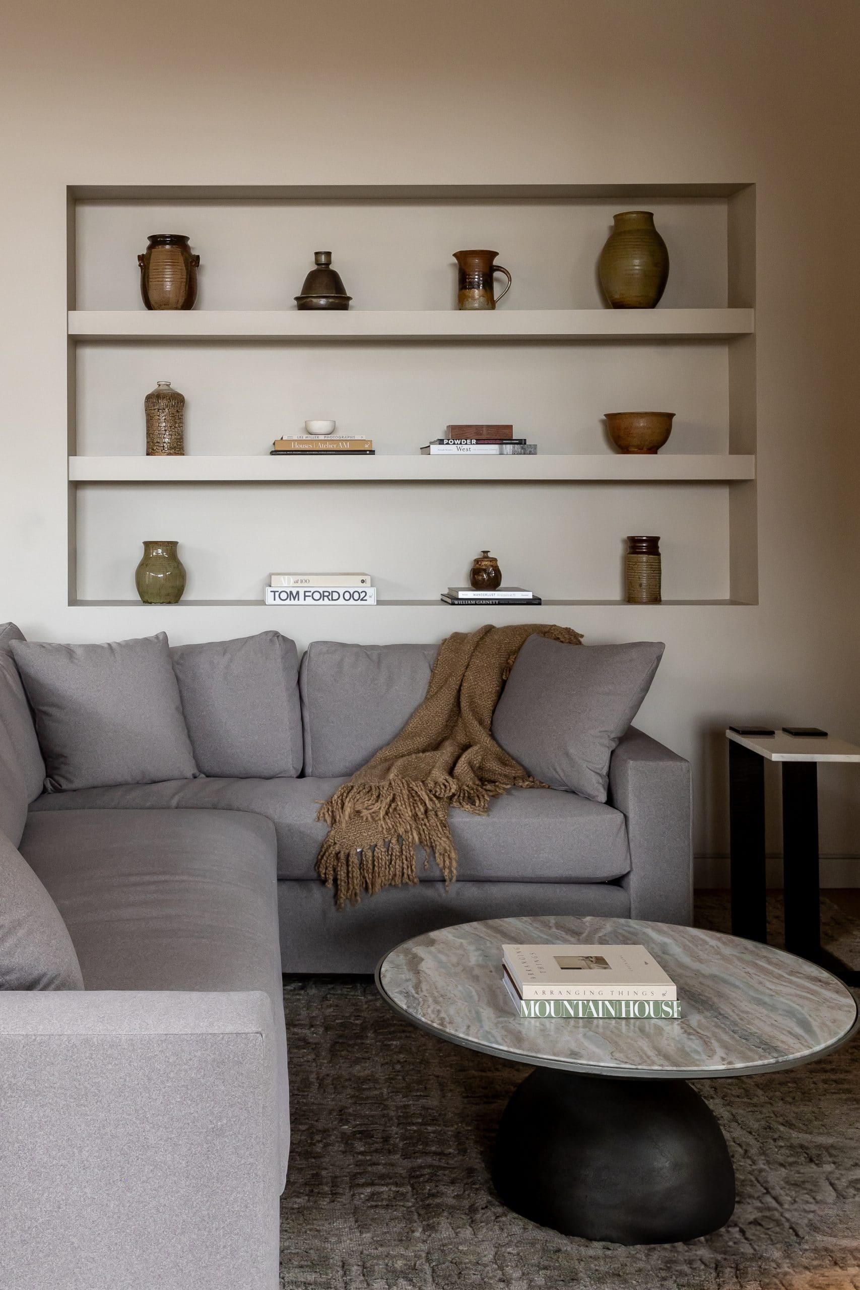 Recessed shelves styled with earthenware pottery above a gray sofa with a woven throw and stone coffee table