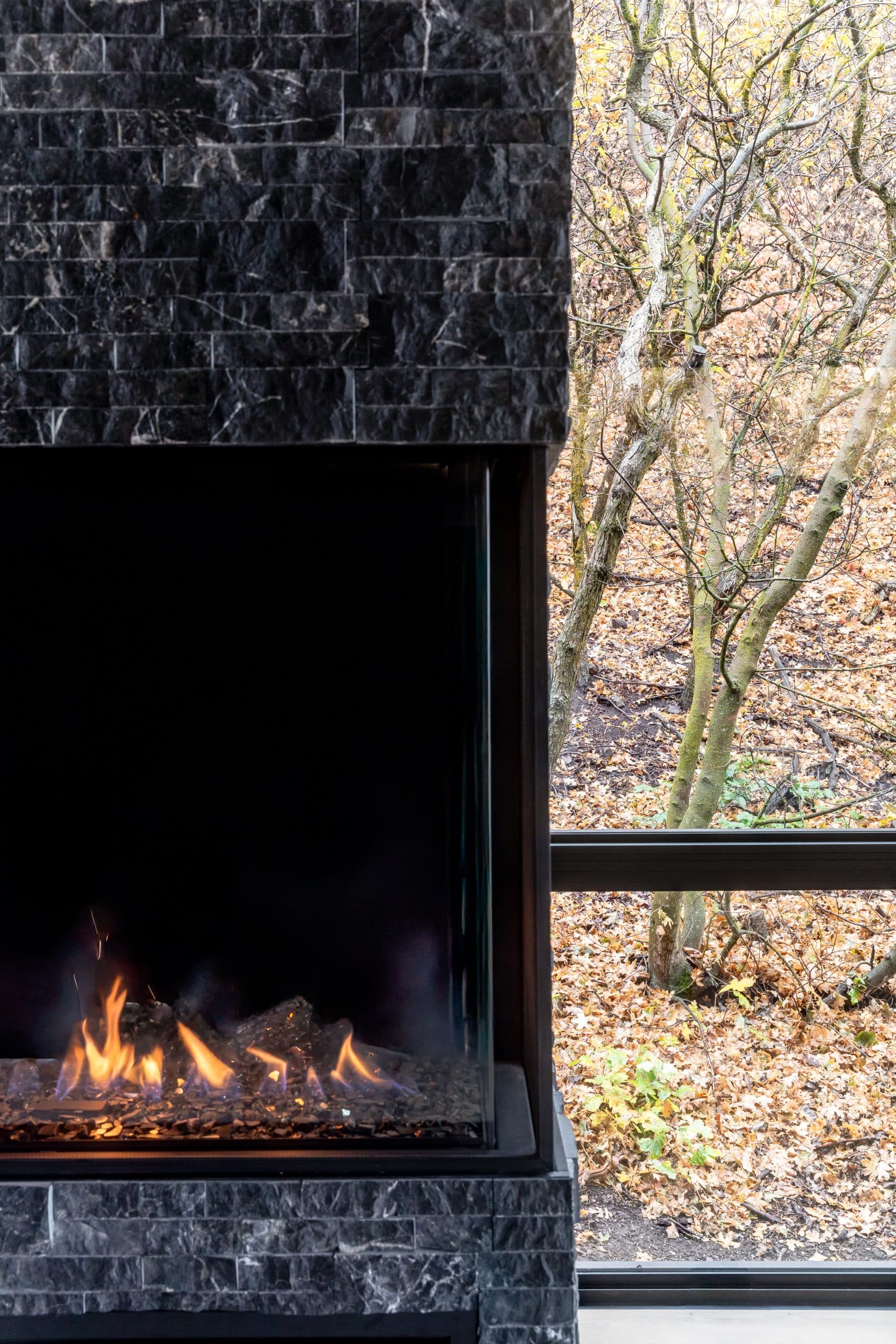 Detail of the black stacked-stone fireplace and firebox against a window onto bare trees