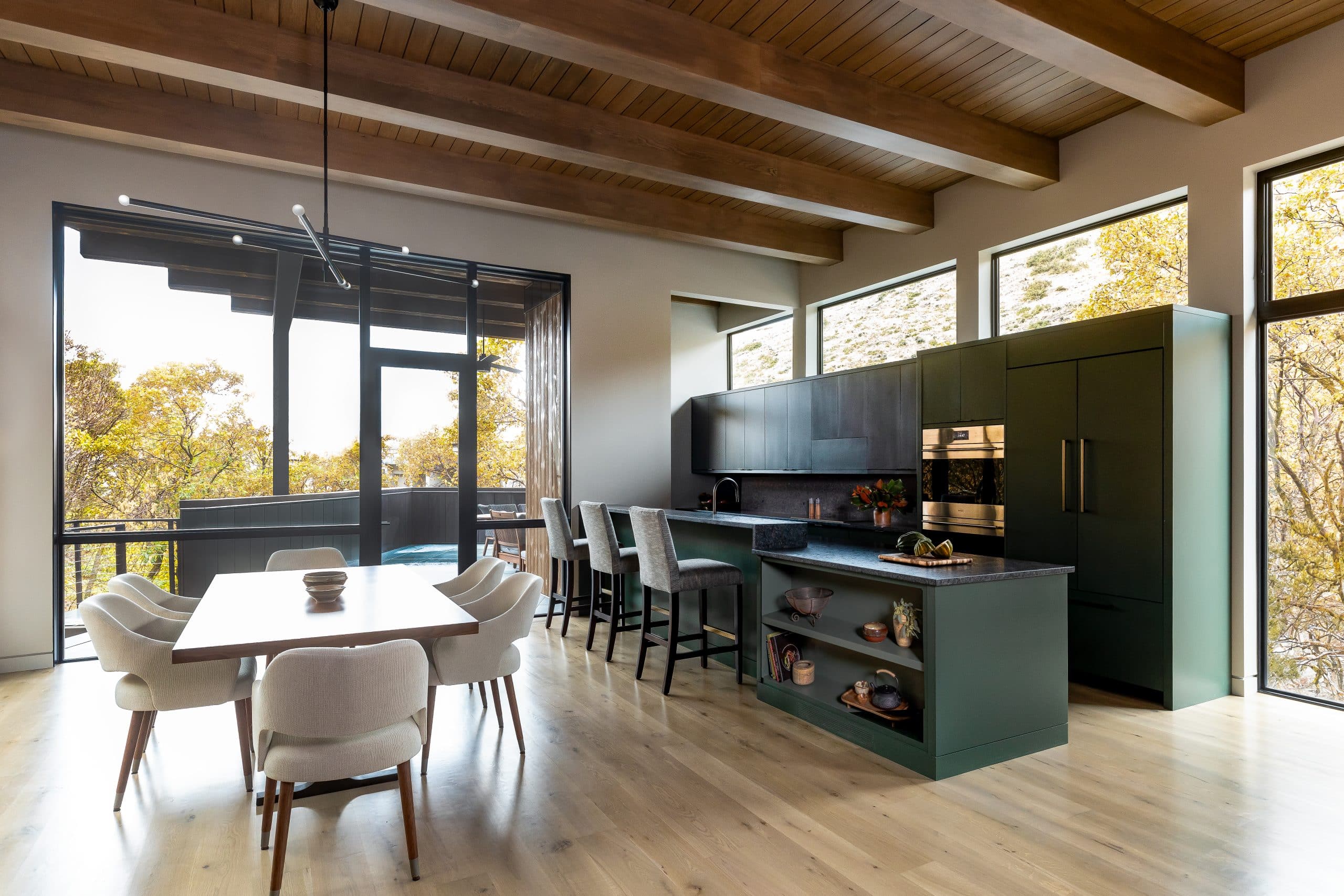 Kitchen and dining space with a deep green island and cabinetry, brass oven, and forest views