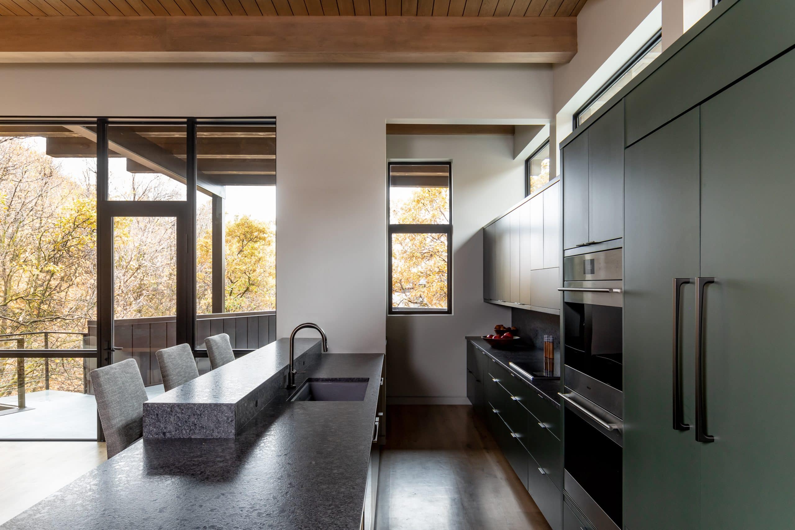 Galley kitchen with a dark stone island, green cabinetry, and windows over the deck