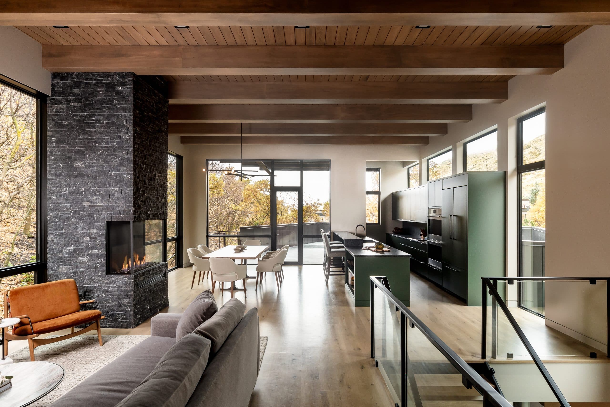 Open-plan living, dining, and kitchen with a green island, leather chair, and glass stair rail