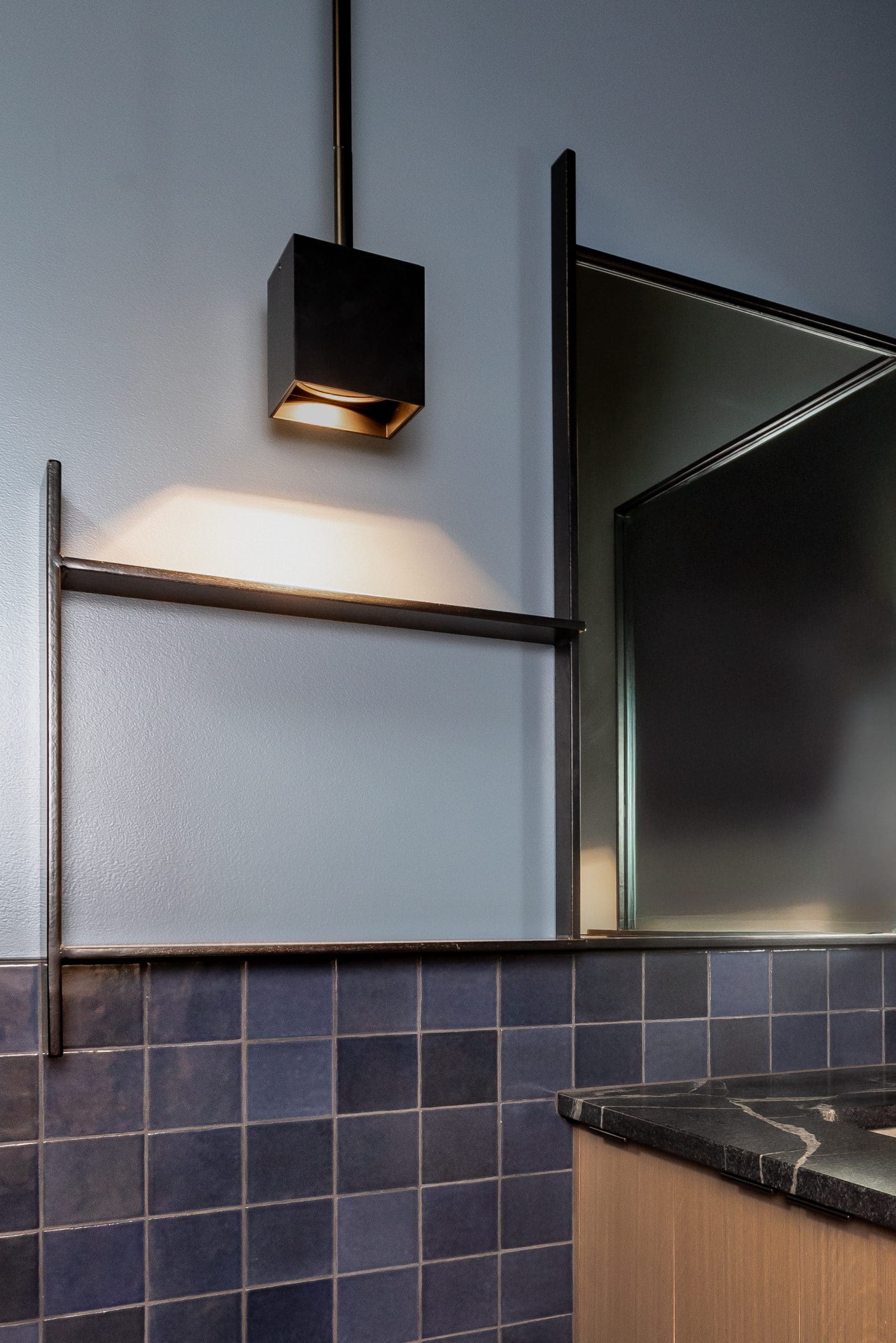 Powder room detail with a black cube pendant, blue tile wainscot, and a stone-topped vanity