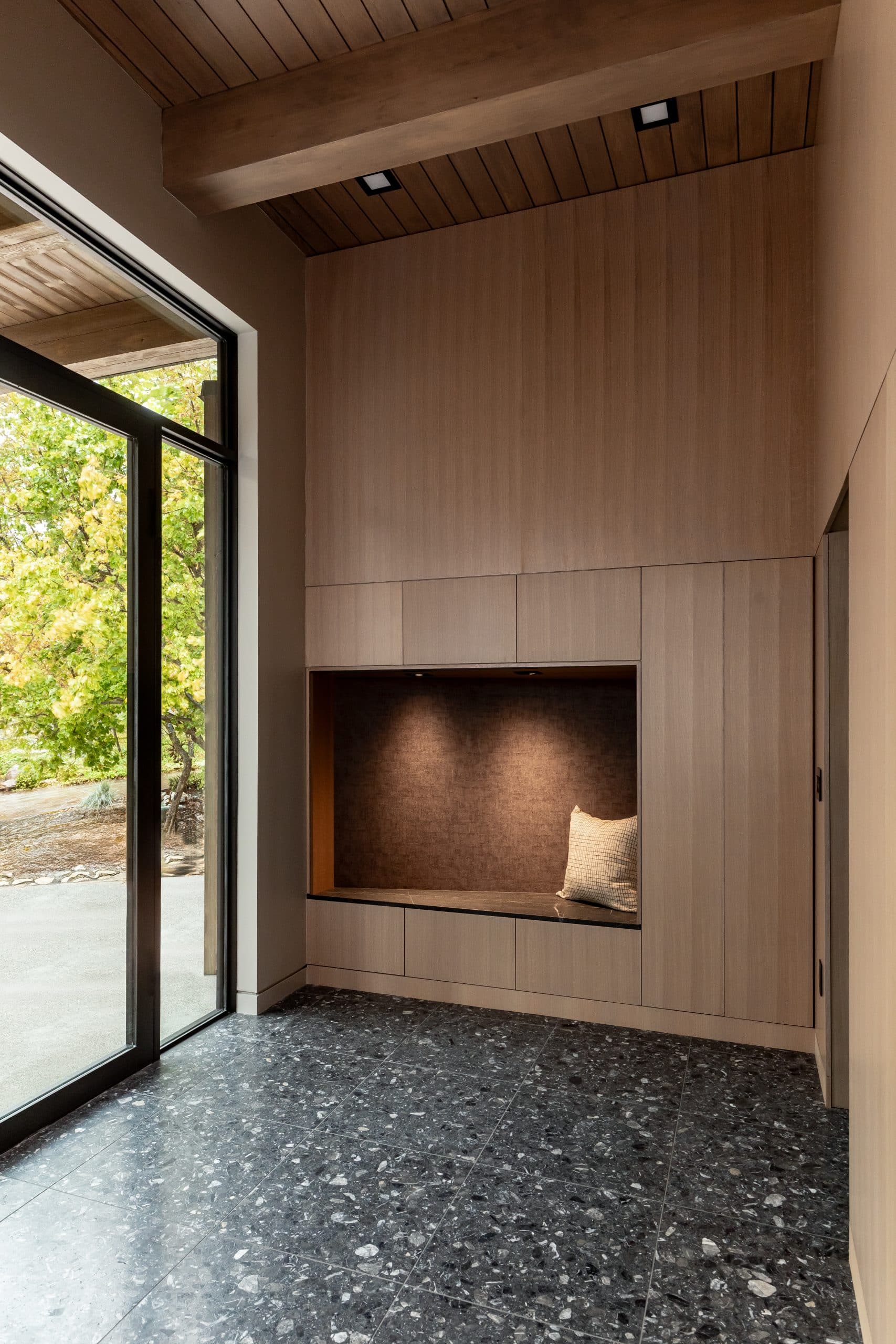 Reading nook with a built-in oak bench and cushion set into a wood-paneled wall beside a sliding glass door
