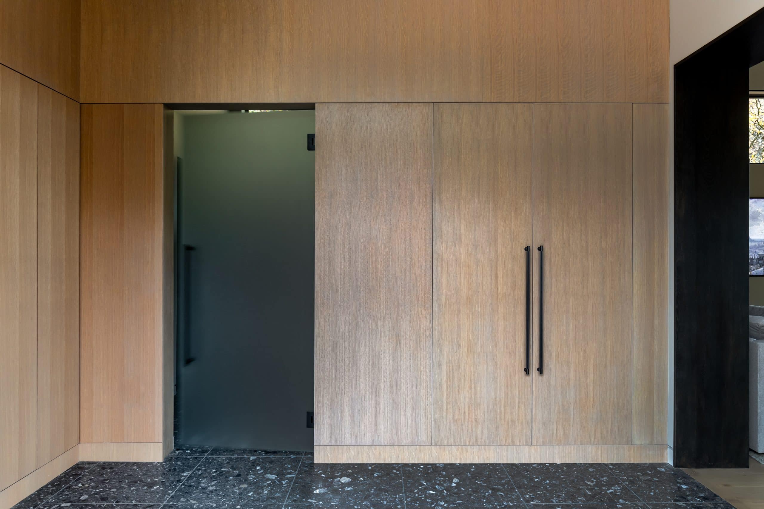 Oak-paneled hall with a concealed doorway and dark terrazzo flooring