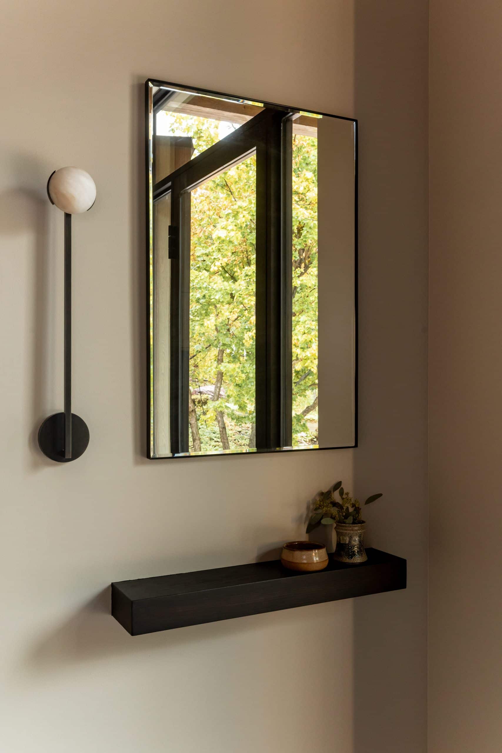 Corner vignette with a globe sconce, a black-framed mirror, and a floating shelf with pottery