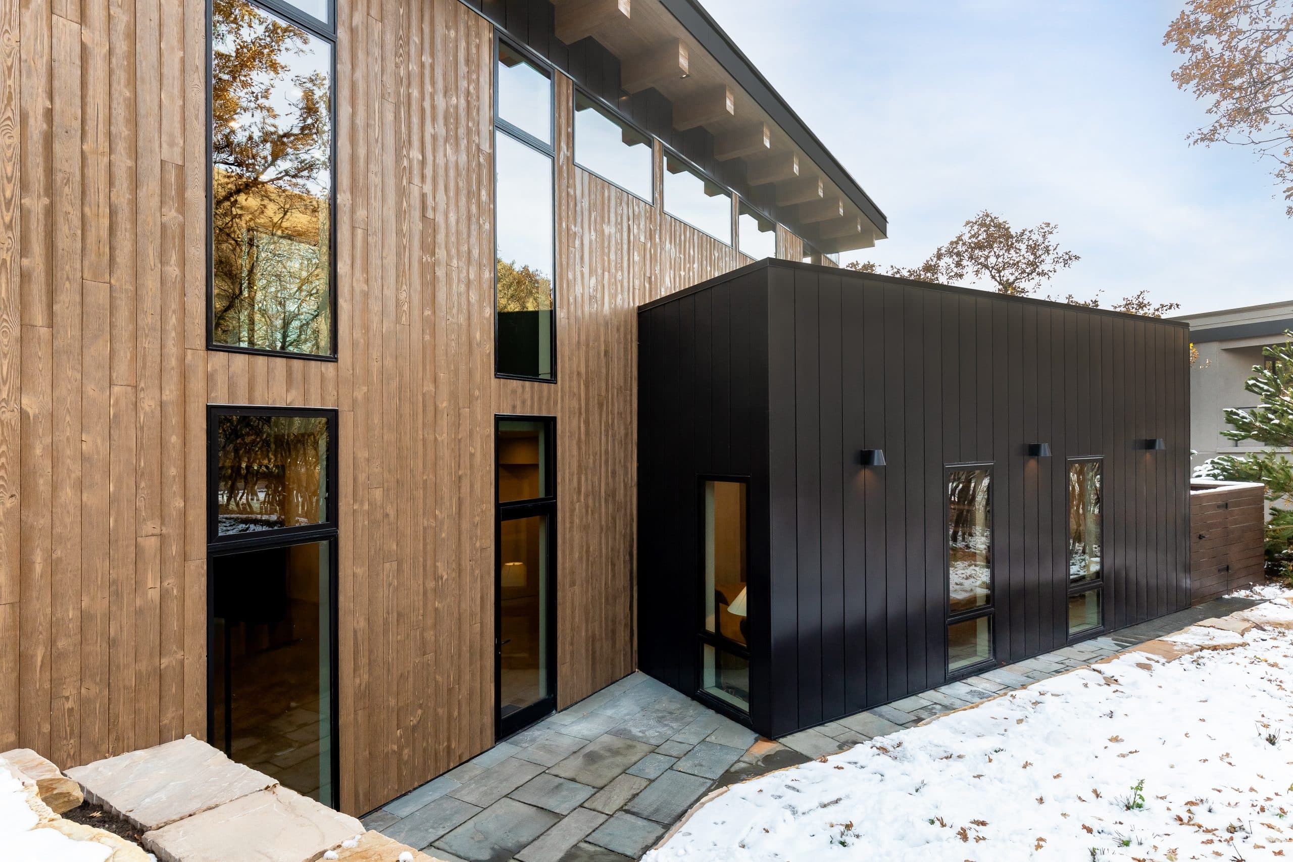 Exterior detail of the vertical wood siding meeting a black-clad wing with a stone-paved path