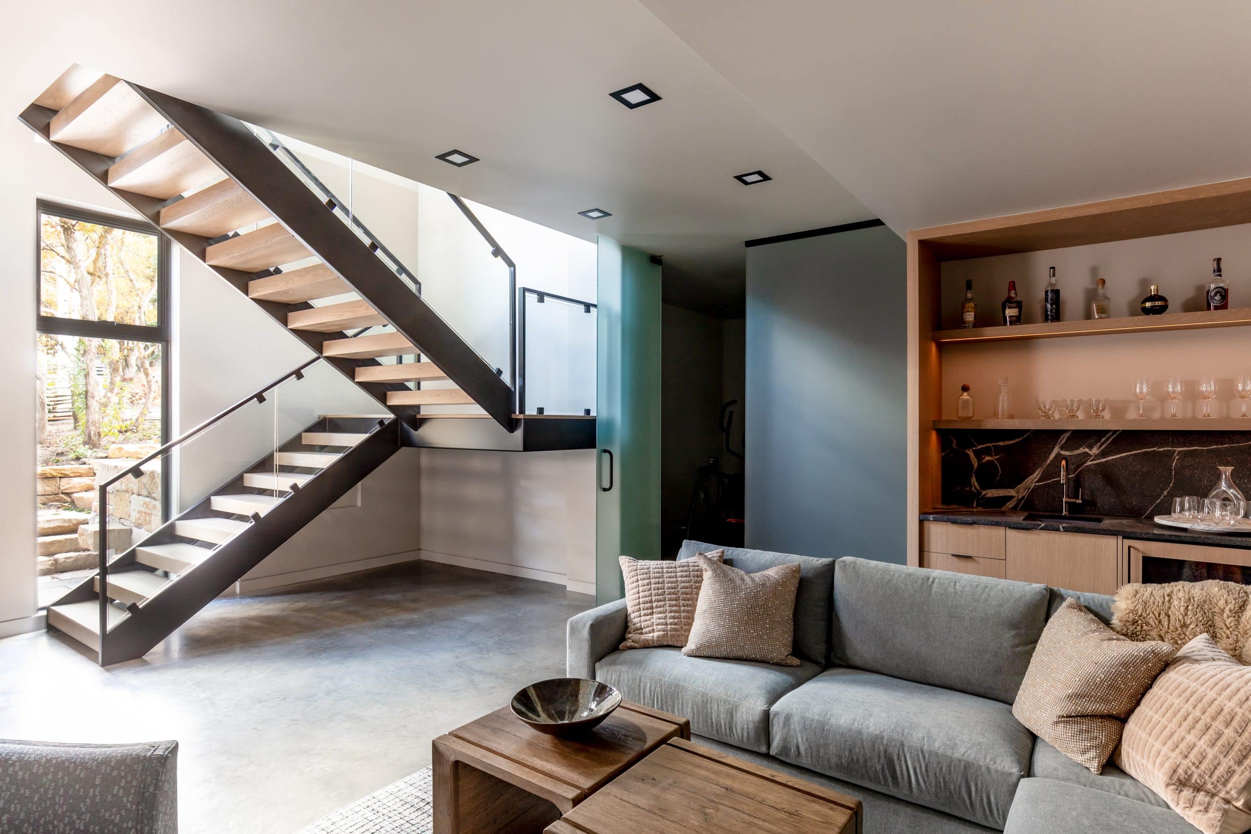Lower-level lounge with the floating staircase, a wet bar, and a gray sectional with a wood coffee table