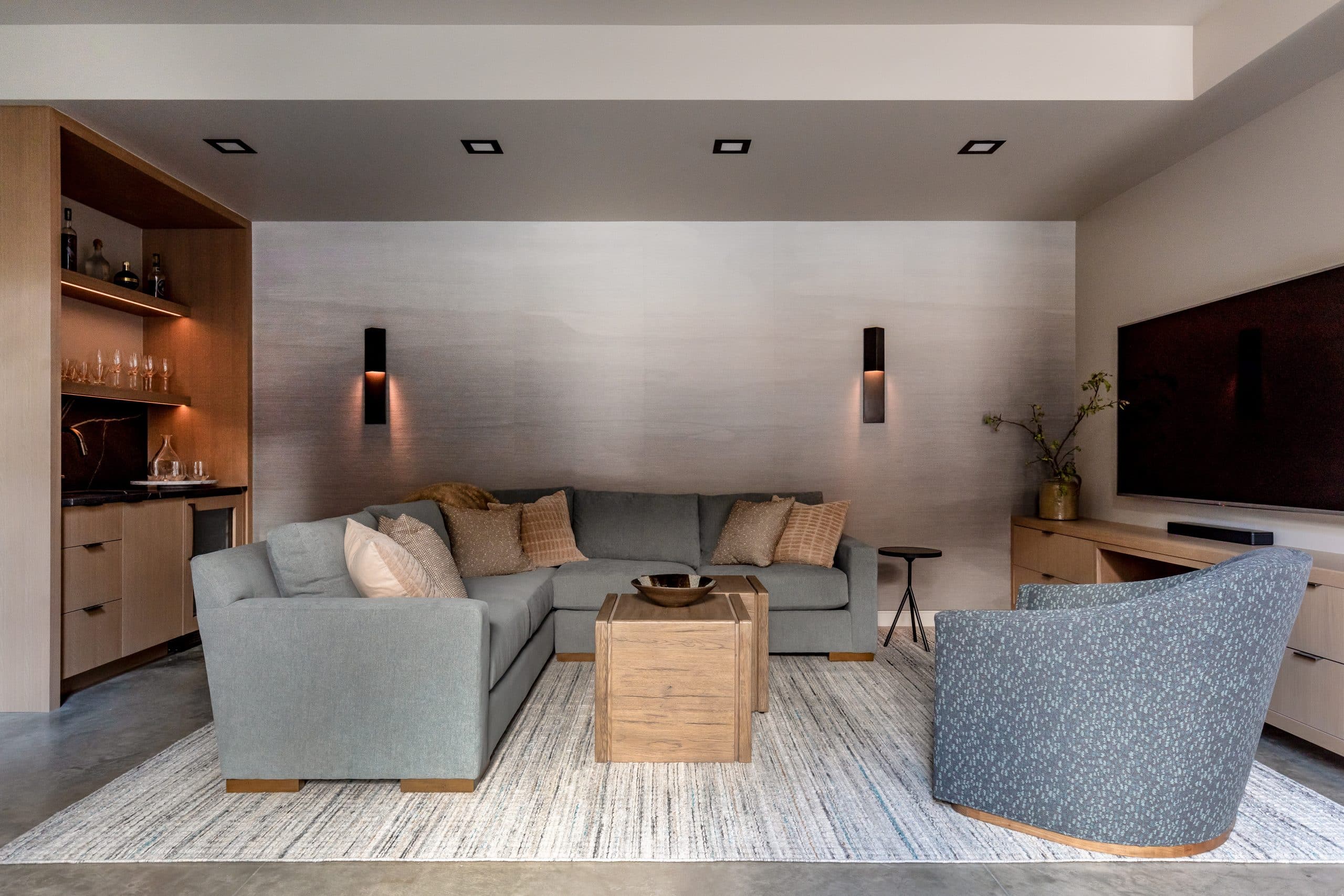 Media room with sectional seating, a wall-mounted television, and linear black sconces