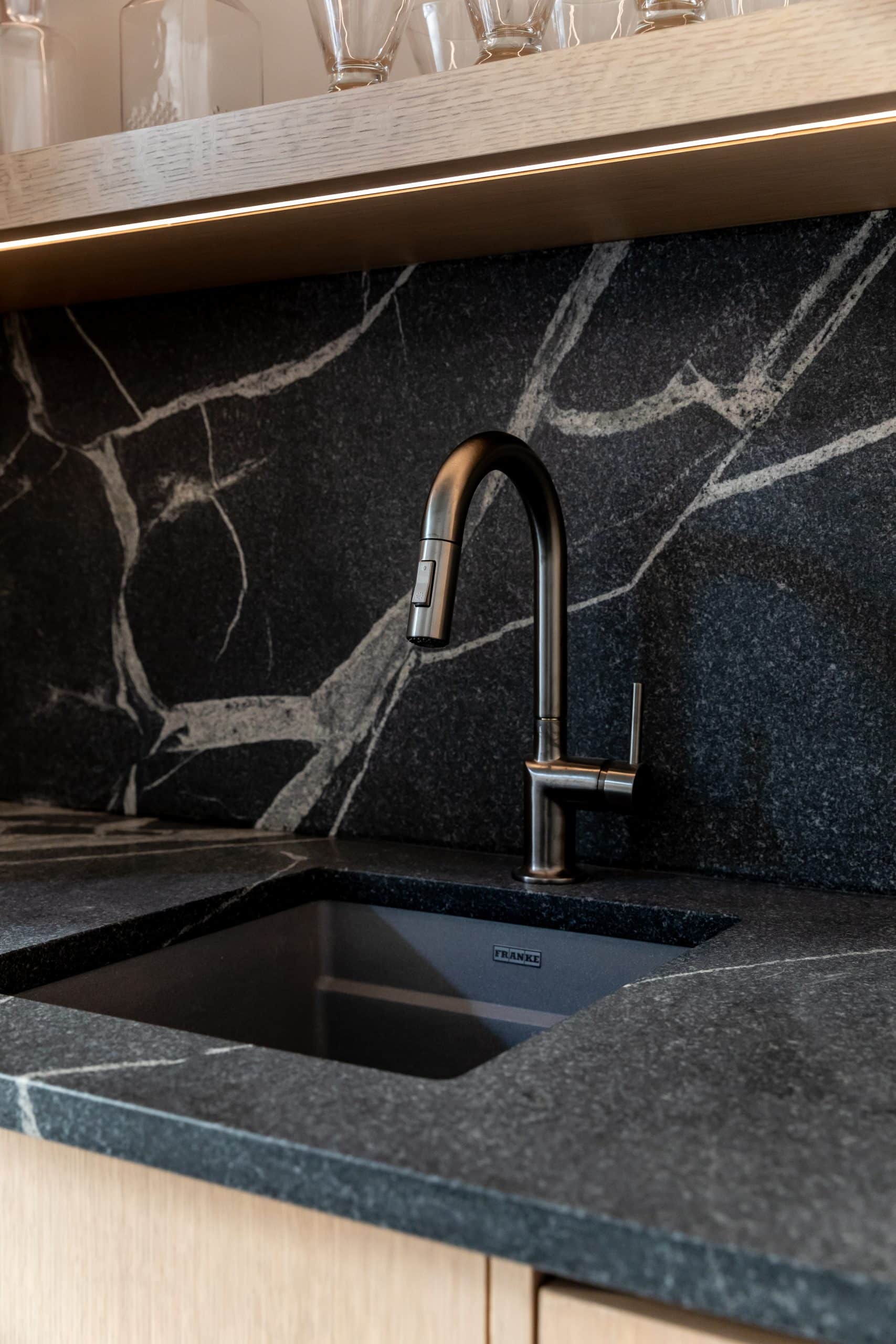 Wet bar detail with a black veined stone backsplash and countertop and an undermount sink